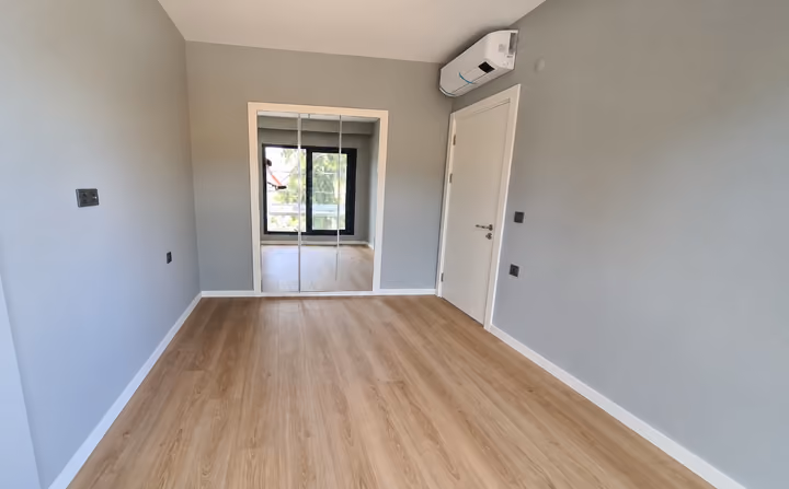 Photograph of an unfurnished room with wood flooring, a mirrored wardrobe and wall-mounted air conditioning.